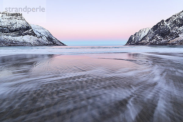 Das rosa Licht des Sonnenaufgangs über den Wellen des gefrorenen Meeres  umgeben von schneebedeckten Gipfeln  Ersfjord  Senja  Troms  Norwegen  Skandinavien  Europa
