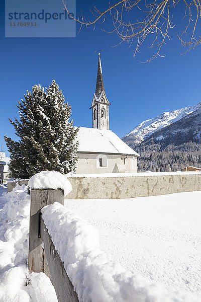 Schneebedeckte Alpenkirche  umrahmt von blauem Himmel  Cinuos  Kanton Graubünden  Engadin  Schweiz  Europa