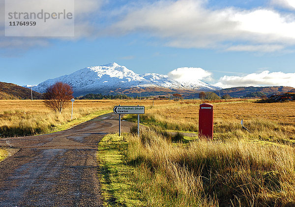 Winteransicht einer roten Telefonzelle und einer Straße in Richtung des schneebedeckten Berges Beinn Resipol in den Mooren der schottischen Highlands  Schottland  Vereinigtes Königreich  Europa