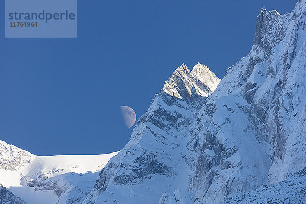 Blauer Himmel und Mond auf den schneebedeckten Graten der hohen Gipfel  Soglio  Bergell  Kanton Graubünden  Schweiz  Europa