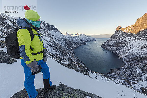 Wanderer auf dem Gipfel des Kammes bewundert das Dorf Fjordgard  eingerahmt vom gefrorenen Meer des Ornfjorden  Senja  Troms  Norwegen  Skandinavien  Europa