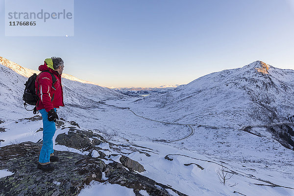 Wanderer auf dem felsigen Kamm bewundert die schneebedeckten Gipfel des Fjordbotn  Lysnes  Senja  Troms  Norwegen  Skandinavien  Europa