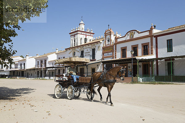 Pferd und Kutsche fahren auf Sandstraßen mit Bruderschaftshäusern im Hintergrund  El Rocio  Provinz Huelva  Andalusien  Spanien  Europa