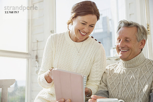 Lächelndes reifes Paar mit digitalem Tablett auf der sonnigen Veranda