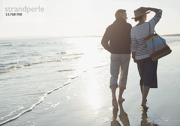 Reife Paare  die am sonnigen Meeresstrand spazieren gehen
