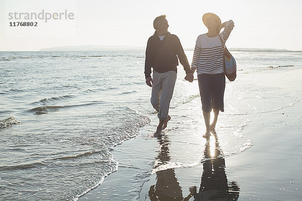Zärtliches  reifes Paar  das sich an den Händen hält und am Sonnenuntergang am Strand spazieren geht.