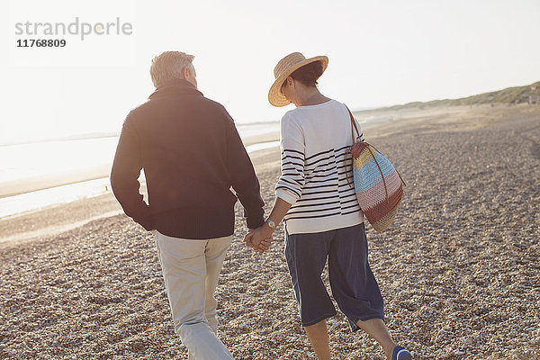 Zärtliches  reifes Paar  das Händchen hält und am sonnigen Strand spazieren geht.