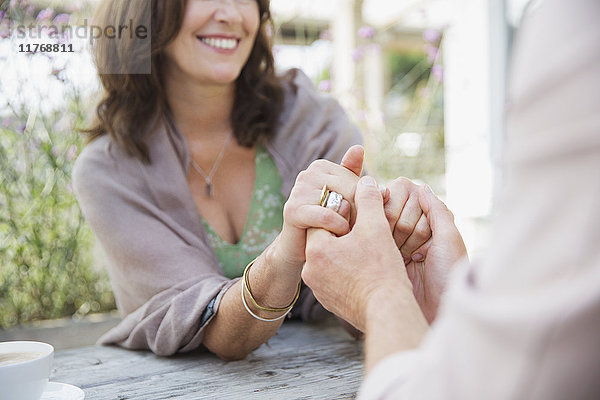 Nahaufnahme eines anhänglichen  reifen Paares  das sich an einem Terrassentisch an den Händen hält.