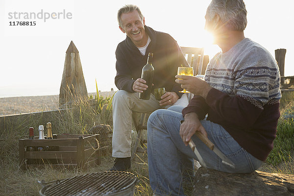 Senioren trinken Wein und grillen am Strand bei Sonnenuntergang