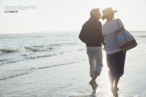 Barfuss reifes Paar  das am Strand bei Sonnenuntergang spazieren geht.