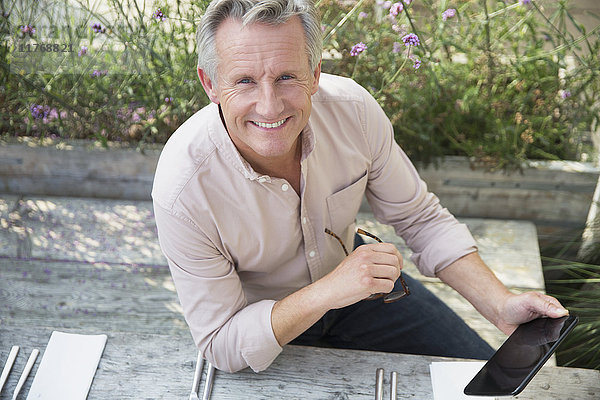 Portrait lächelnder älterer Mann mit digitalem Tablett auf der Terrasse