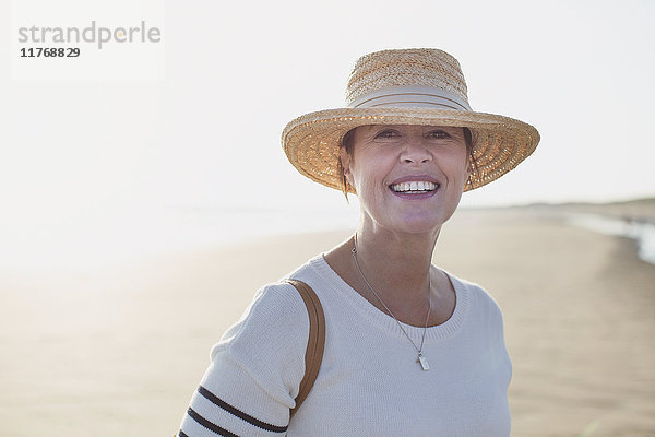 Portrait lächelnde reife Frau mit Strohhut am sonnigen Sommerstrand
