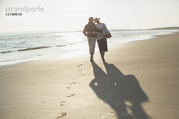 Zärtliches  reifes Paar  das sich umarmt und am sonnigen Strand spazieren geht.