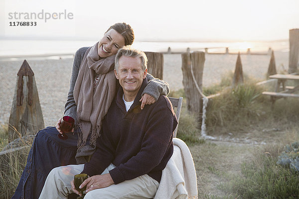 Portrait liebevolles reifes Paar beim Weintrinken am Strand bei Sonnenuntergang