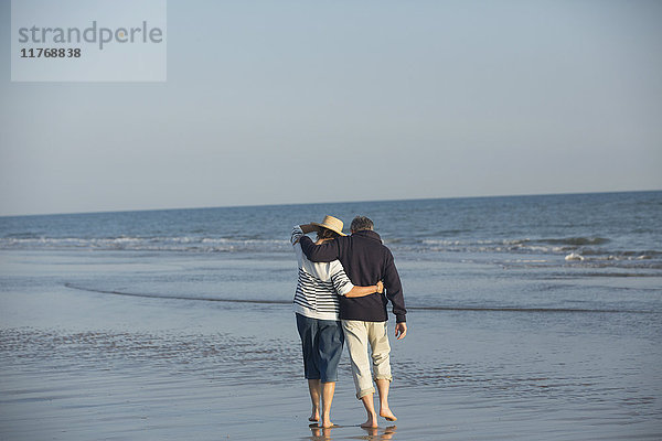 Zärtliches  reifes Paar  das sich umarmt und in der sonnigen Meeresbrandung spazieren geht.