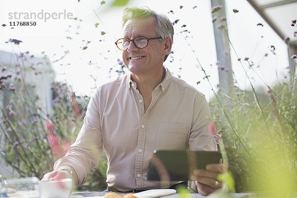 Lächelnder älterer Mann mit digitalem Tablett auf der sonnigen Terrasse