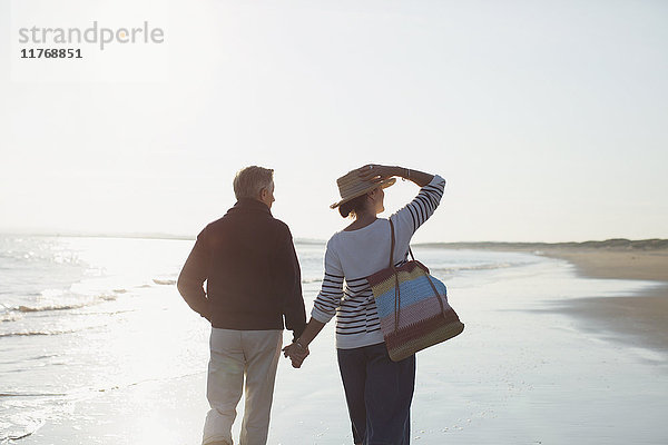 Zärtliches  reifes Paar  das sich an den Händen hält und am sonnigen Strand spazieren geht.