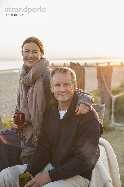Portrait lächelndes reifes Paar beim Weintrinken am Strand bei Sonnenuntergang