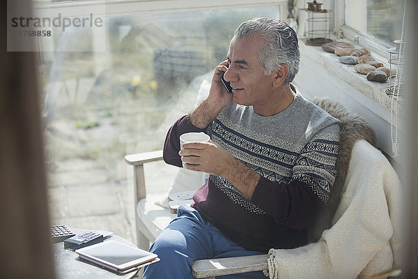 Senior Mann trinkt Kaffee und telefoniert auf der Veranda.