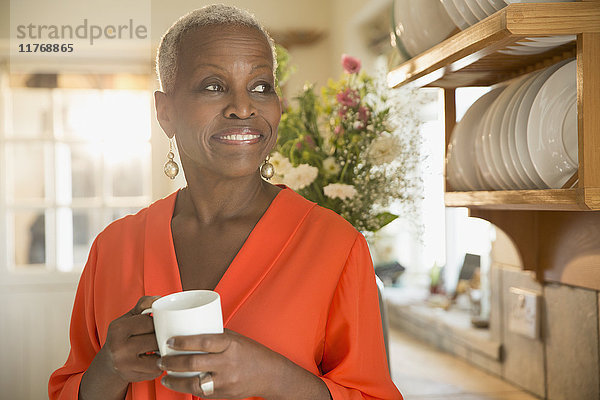 Lächelnde Seniorin beim Kaffeetrinken in der Küche