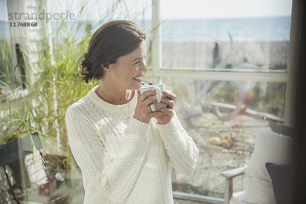 Lächelnde reife Frau trinkt Kaffee am Strand Haus Sonne Veranda