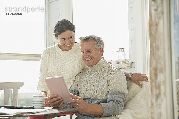 Lächelndes reifes Paar mit digitalem Tablett am Tisch auf der Sonnenterrasse
