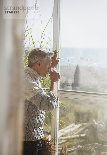 Senior Mann trinkt Kaffee am sonnigen Strandhausfenster