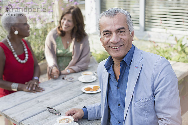 Portrait lächelnder älterer Mann beim Kaffeetrinken mit Freunden am Terrassentisch