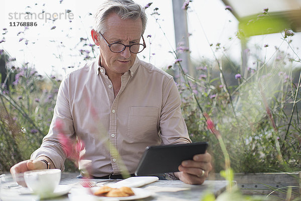 Senior Mann mit digitaler Tablette und Kaffee trinken auf der Terrasse Tisch