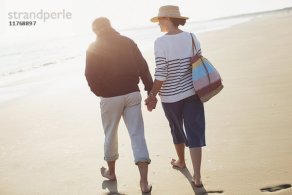 Barfuß reifes Paar  das sich an den Händen hält und am sonnigen Strand spazieren geht.