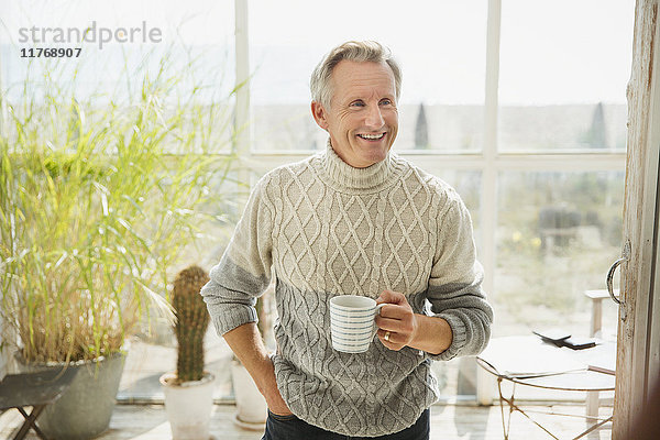 Lächelnder reifer Mann trinkt Kaffee am sonnigen Strand Haus Sonne Veranda