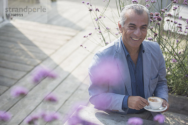 Portrait lächelnder älterer Mann beim Kaffeetrinken auf der Sonnenterrasse