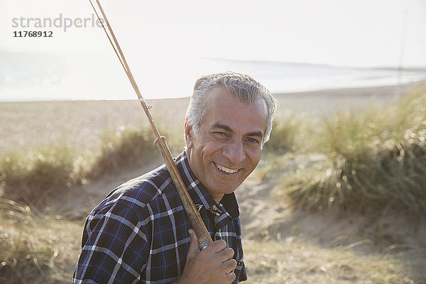 Portrait lächelnder älterer Mann mit Angelrute am sonnigen Strand