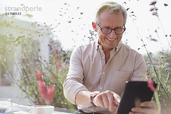 Lächelnder älterer Mann mit digitalem Tablett auf der Terrasse