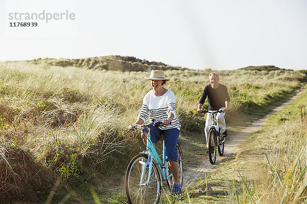 Reife Paare beim Fahrradfahren auf dem sonnigen Strandgrasweg