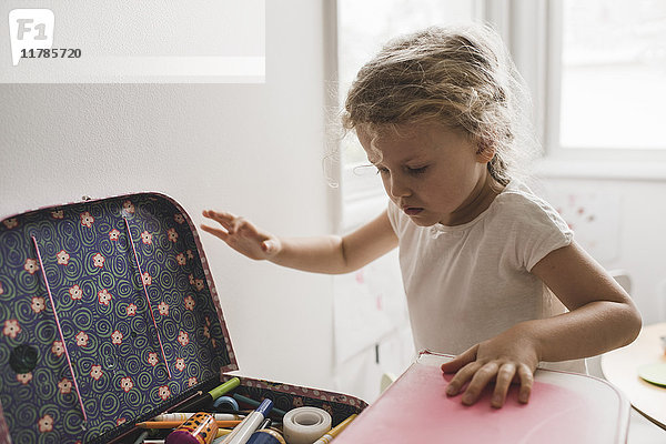 Mädchen auf der Suche nach Spielzeug im Koffer im Spielzimmer