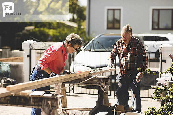 Seniorenpaar beim Vermessen von Holzbrettern auf dem Hof
