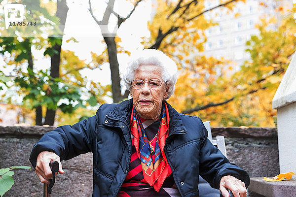 Porträt einer selbstbewussten Seniorin  die im Herbst im Park sitzt.