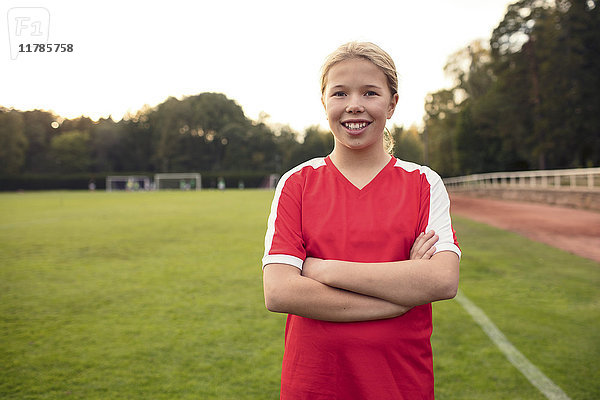 Porträt einer fröhlichen Fußballspielerin  die mit gekreuzten Armen auf dem Feld steht.