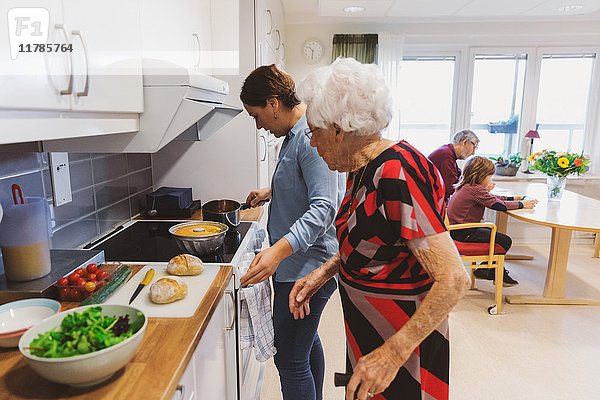 Seitenansicht von Seniorin und Tochter beim Kochen in der Küche