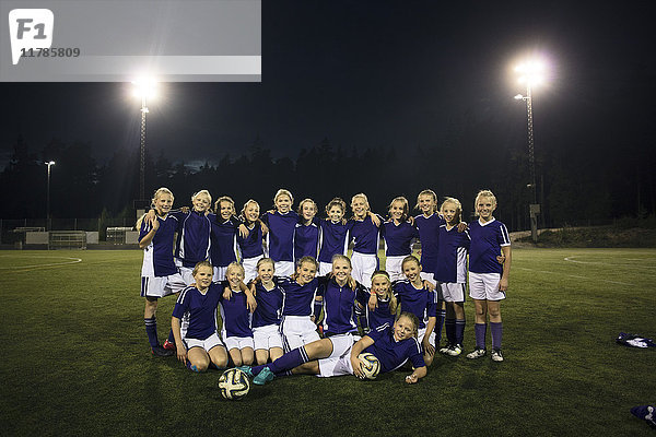 Porträt der Mädchenfußballmannschaft auf dem beleuchteten Feld gegen den Himmel