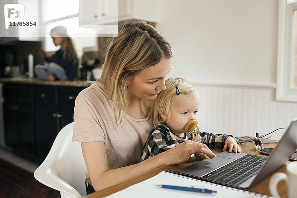 Mittlere erwachsene Frau  die den Laptop benutzt  während ihre Tochter zu Hause auf dem Schoß sitzt.