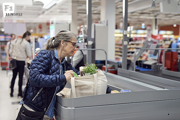 Reife Frau beim Einkaufen an der Kasse im Supermarkt