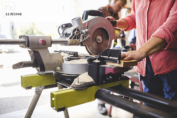 Mittelteil der Seniorin beim Schneiden von Holzbrettern mit Kreissäge in der Werkstatt