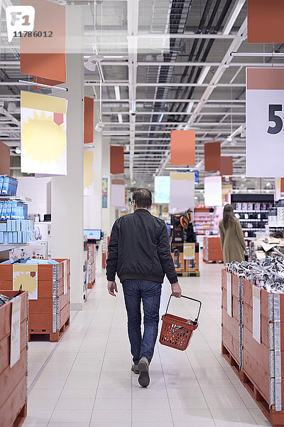 Rückansicht des Mannes  der den Korb trägt  während er im Supermarkt spazieren geht.