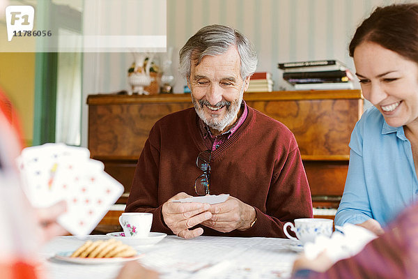 Glücklicher älterer Mann  der mit seiner Familie zu Hause Karten spielt.