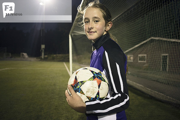 Porträt des Mädchens mit Fußball gegen den Torpfosten stehend