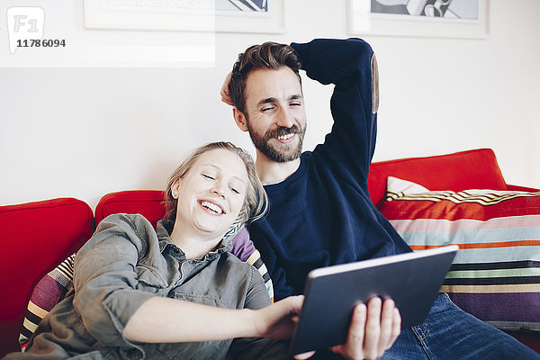 Glücklich  dass ein Paar auf dem Sofa im Wohnzimmer auf ein digitales Tablett schaut.