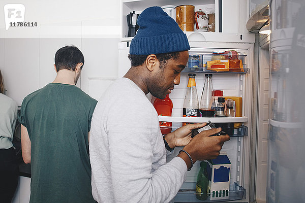 Seitenansicht des Mannes beim Betrachten der Lebensmittelverpackung am Kühlschrank in der Küche