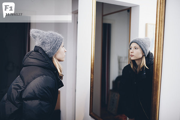 Frau betrachtet Spiegelung im Spiegel an der Wand